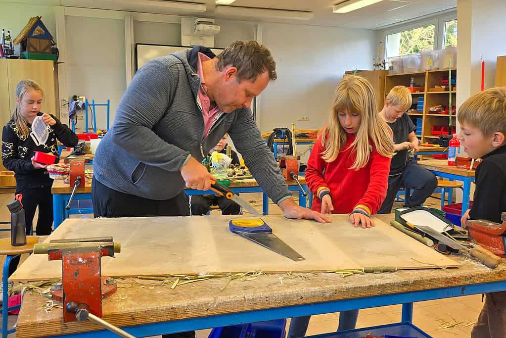 Lehrer zeigt Kindern in der Holzwerkstatt kreative Holzarbeiten in Zingst.